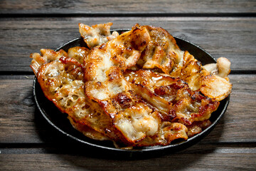 Fried bacon in a pan with spices.