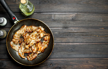 Fried bacon in a pan with spices.