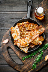 Fried bacon in a pan with spices and rosemary.