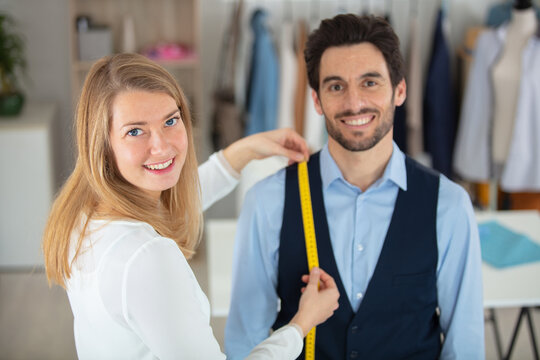 young tailor taking measurements of male customer