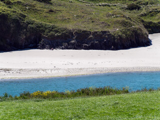 Shrub-covered sand dunes on the shore of the Atlantic Ocean on a spring day. Green grass covered mountain beside blue sea