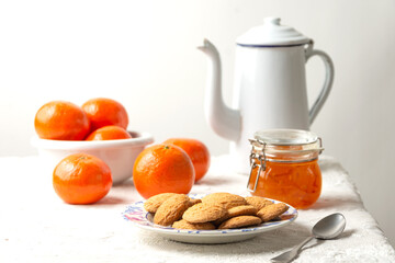 Close up of cookies, old fashioned coffee pot, jam, spoon and tangerines on white tablecloth, white background, horizontal with copy space