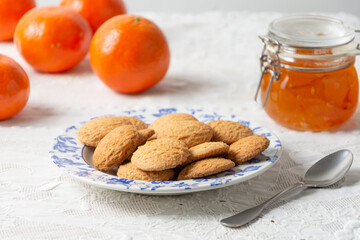 Close-up of cookies, jam jar, spoon and tangerines on white tablecloth, horizontal with copy space