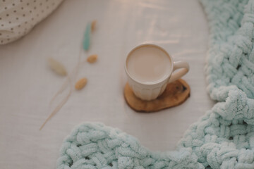 Cup of coffee with milk on the bed with white linens and blanket. Morning coffee in bed concept.