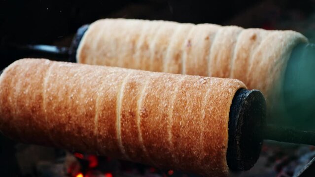 Preparation of the Hungarian and Romanian traditional Christmas bread, chimney cake, kurtos kalacs trdelnik roasted over charcoal in market. German and Hungarian sweet specialty made in Budapest.