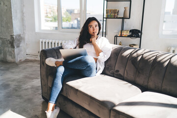 Thoughtful woman sitting on sofa with laptop in living room