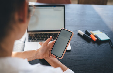 Crop businesswoman typing on computer while using phone