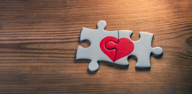 Closeup of two pieces of a puzzle with red heart on wooden   background.