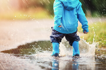 Small child jumping through puddles in nature in spring