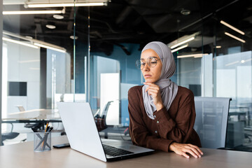 Serious bored businesswoman inside office, muslim woman in hijab thinking while sitting at...