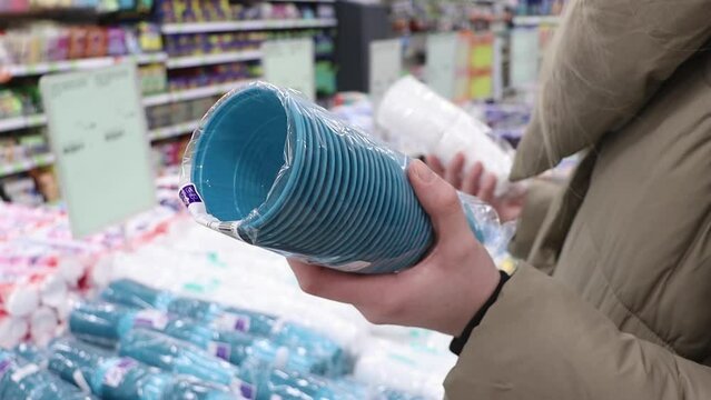 The customer chooses plastic cups in the store. Disposable tableware