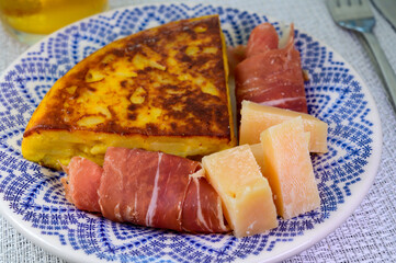 Spanish food, portion of potato omelette tortilla de patatas with onion served with cheese and jamon