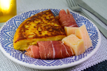 Spanish food, portion of potato omelette tortilla de patatas with onion served with cheese and jamon