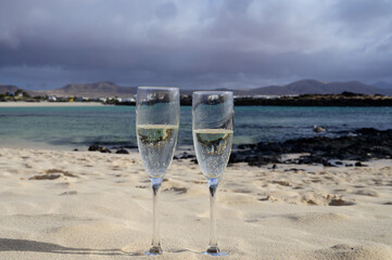 Two glasses of white champagne or cava sparkling wine served on white sandy tropical beach and blue ocean, romantic vacation, winter sun on Fuerteventura, Canary, Spain