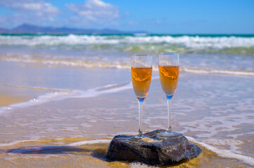 Two glasses of rose champagne or cava sparkling wine served on white sandy tropical beach and blue ocean water, romantic vacation, winter sun on Fuerteventura, Canary, Spain