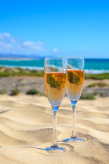 Two glasses of rose champagne or cava sparkling wine served on white sandy tropical beach with dunes and blue ocean, romantic vacation, winter sun on Fuerteventura, Canary, Spain