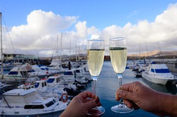 Obraz premium Everyday party, hands with glasses of cava or champagne sparkling wine in yacht harbour of Caleta Fuste, Fuerteventura, Canary islands vacation, Spain