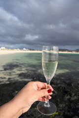 Hand with glass of white champagne or cava sparkling wine on white sandy tropical beach and blue ocean, romantic vacation, winter sun on Fuerteventura, Canary, Spain