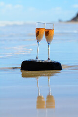 Two glasses of rose champagne or cava sparkling wine served on white sandy tropical beach and blue ocean water, romantic vacation, winter sun on Fuerteventura, Canary, Spain
