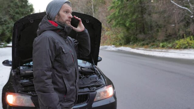 Car broken down by roadside with hazard lights and hood open, man on cellphone calling for help, tow truck. 4K 24FPS