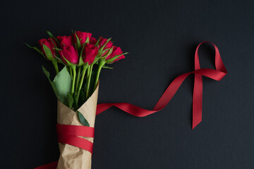 Bouquet of red roses with decorative ribbon on black cardboard background. Copy space.