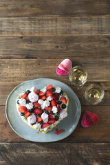 Heart-shaped cake decorated with red fruits and meringue. Rustic wooden background. Valentine's Day. Copy space. Vertical photo.