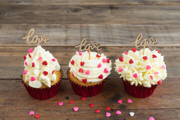 Three cupcakes with red topping decoration and a wooden sign with the word LOVE on a wooden background. Copy space.
