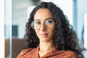 Close-up portrait of confident serious business woman, hispanic woman wearing glasses inside office...