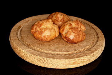 Three fresh chouquettes on a round bamboo tray, on a black background.