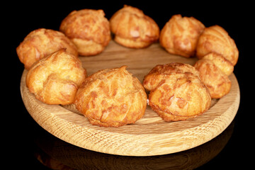 Several fresh mouth-watering Chouquettes on a round bamboo tray, close-up, on a black background.