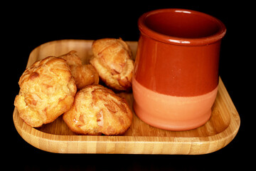 Several sweet Chouquettes on a bamboo plate with a clay glass, close-up, on a black background.