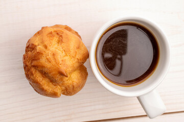 One delicious aromatic chouquettes with a cup of coffee, close-up, on a painted wooden table, top view.