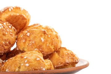 Several sweet chouquettes on a clay plate, close-up, isolated on white.