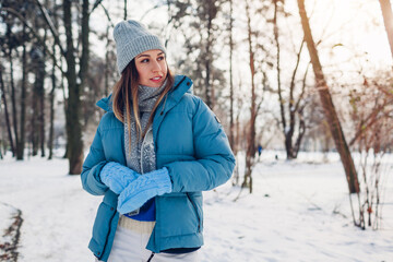 Young woman walking in snowy winter park wearing blue coat. Girl enjoys landscape wearing hat and mittens