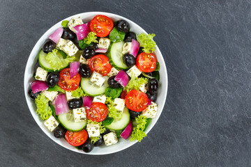 Greek salad with fresh tomatoes olives and feta cheese healthy eating food from above on a slate with copyspace copy space