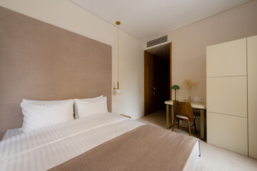 Fototapeta na wymiar comfortable bed with white bedding near desk and wooden chair in modern hotel bedroom.