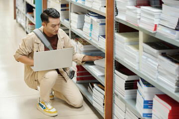 High school student with laptop searching for books for his research in library