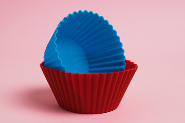 Blue and red silicone molds for cupcakes on a pink paper background