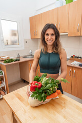 Athletic girl in sportswear holding eco bag with vegetables in a kitchen. Vegan woman. Proper nutrition concept.