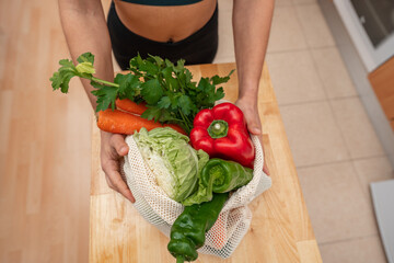 Athletic girl in sportswear holding eco bag with vegetables in a kitchen. Vegan woman. Proper nutrition concept. Top view