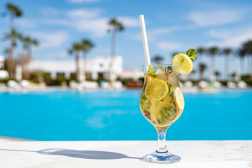 Mohito fresh cold cocktail on the wooden table with eco paper straw in the all inclusive hotel near the swimming pool