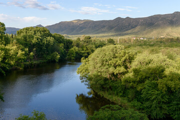 Fototapeta na wymiar Embalse del río en el Valle de Punilla. Arboleda frondosa en la ribera del río.