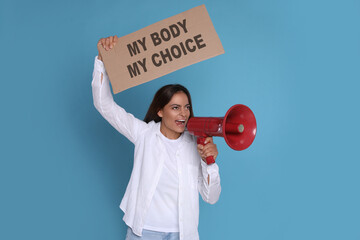 Emotional woman shouting into megaphone and holding placard with phrase My Body My Choice on light...