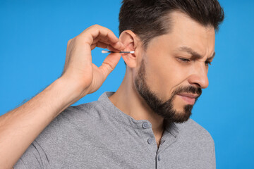 Obraz premium Emotional man cleaning ears on light blue background