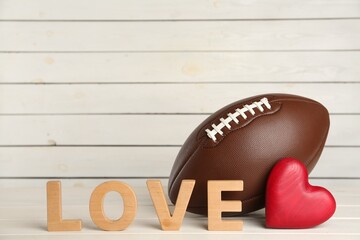 American football ball, heart and word Love on white wooden table. Space for text