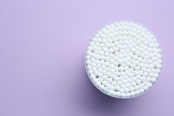 Many cotton buds in container on violet background, top view. Space for text
