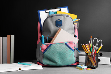 Backpack with different school stationery on grey wooden table near blackboard