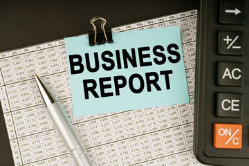 On financial reports lies a calculator, a pen and a sticker with the inscription - BUSINESS REPORT