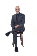 front view of a man sitting  on chair with suit and tie and cross legged smiling  and looking at camera on white background