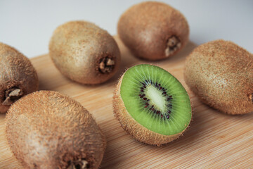 Wooden board with whole kiwis and cut one on beige background, closeup